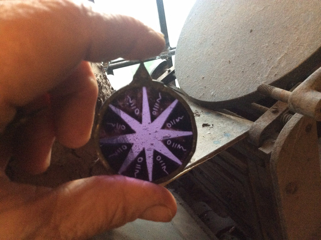 Hand holding a star-shaped object with purple centre and fine details ,against a blurred background of printing press machinery in the studio.
