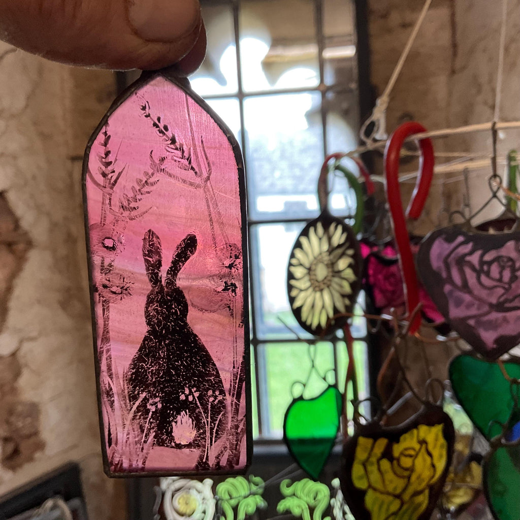 Stained glass piece with a rabbit design held by a hand, surrounded by other colorful glass pieces.