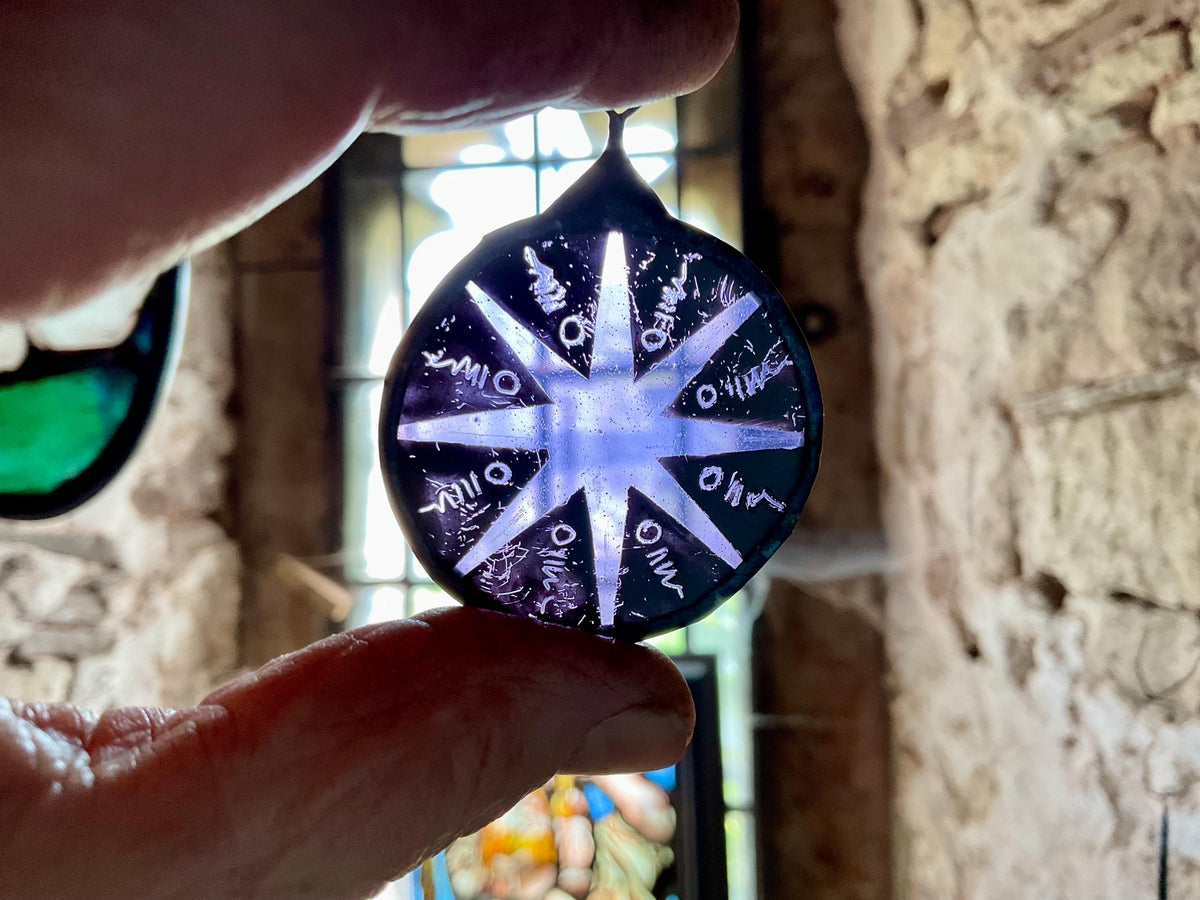 Hand holding a round, painted and kiln fired piece of glass with star-like design against a blurred background