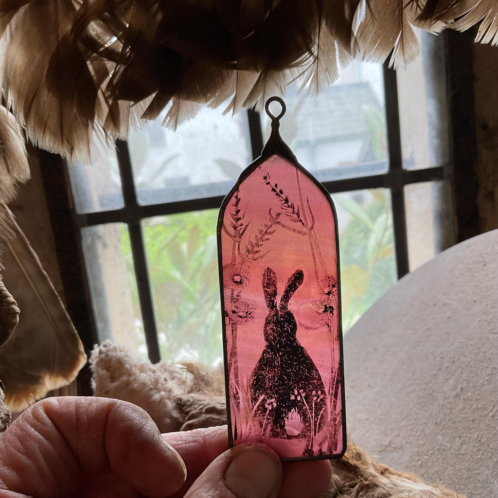 Decorative pink glass sun catcher with a rabbit design held in front of a window.