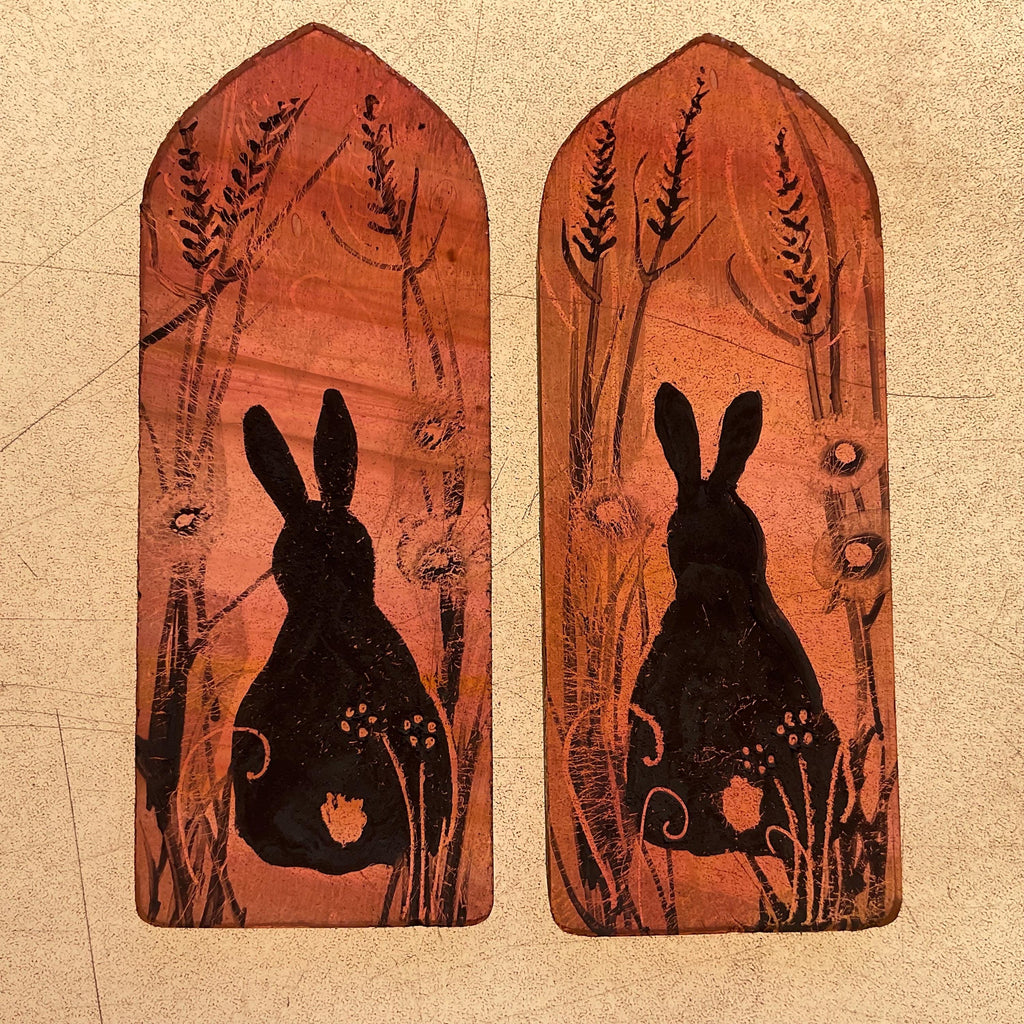 Two stained glass panels with black rabbit silhouettes and nature-themed designs on a light box