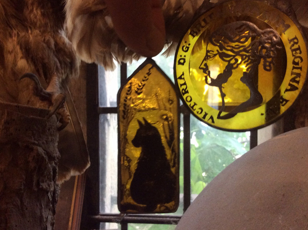 Decorative glass panels with cat silhouette and a coin with  text, from a vintage image shown in a window 