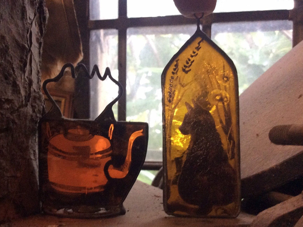 Decorative glass pieces with a cat silhouette and a kettle on a windowsill.