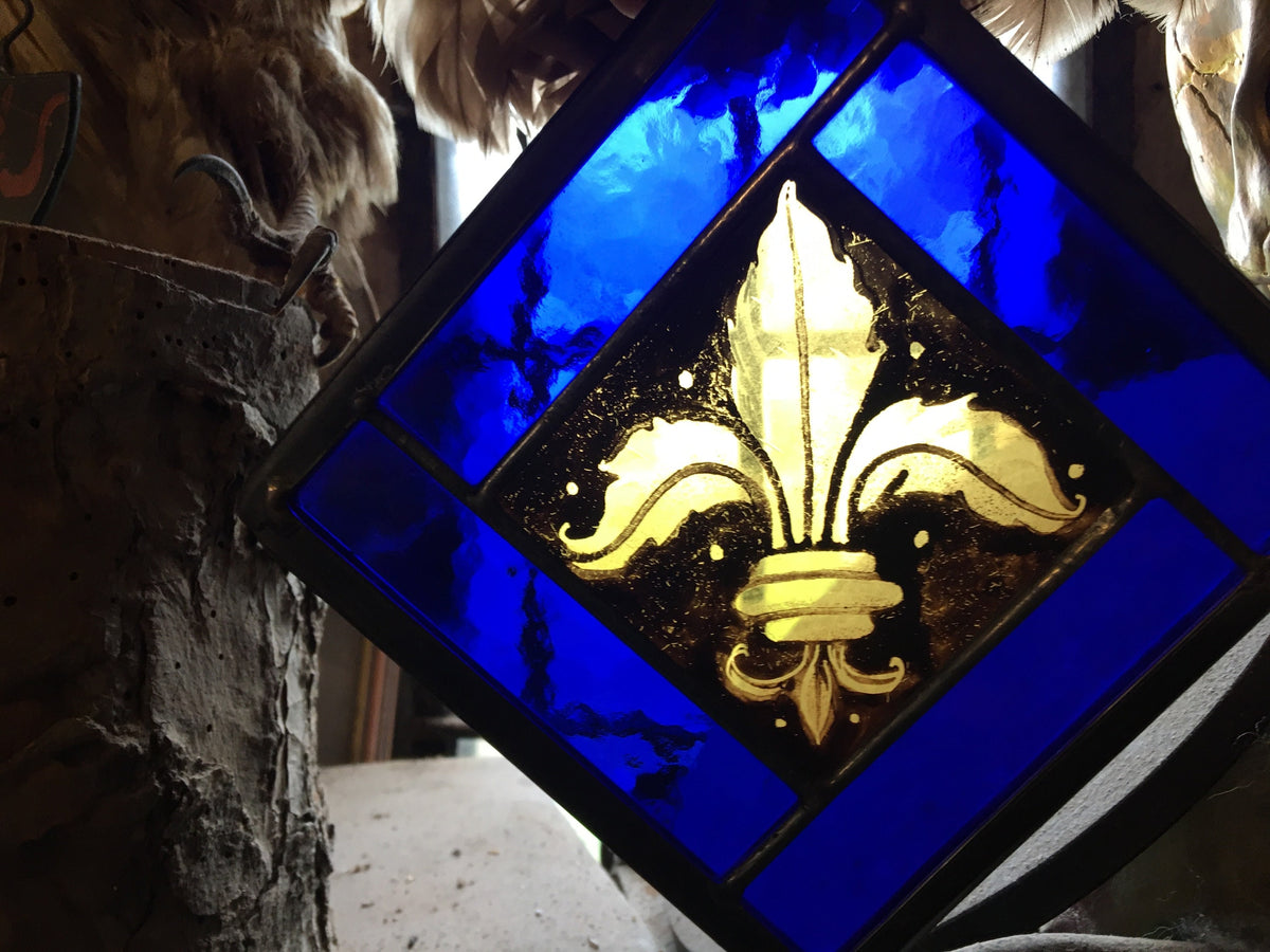 Stained glass panel with gold fleur-de-lis design on a blue background