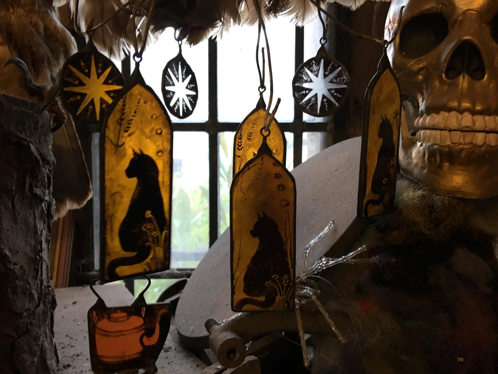 Decorative items with black cats and stars hanging against a window with bars.