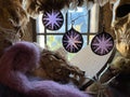 Purple stained glass circles with  star motif sun catchers  hanging in front of a window with decorative elements.