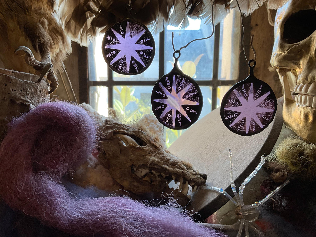 Purple stained glass circles with  star motif sun catchers  hanging in front of a window with decorative elements.