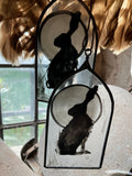 Decorative glass pieces with hare  silhouettes each end backed by a full moon, shown against a window with feathers