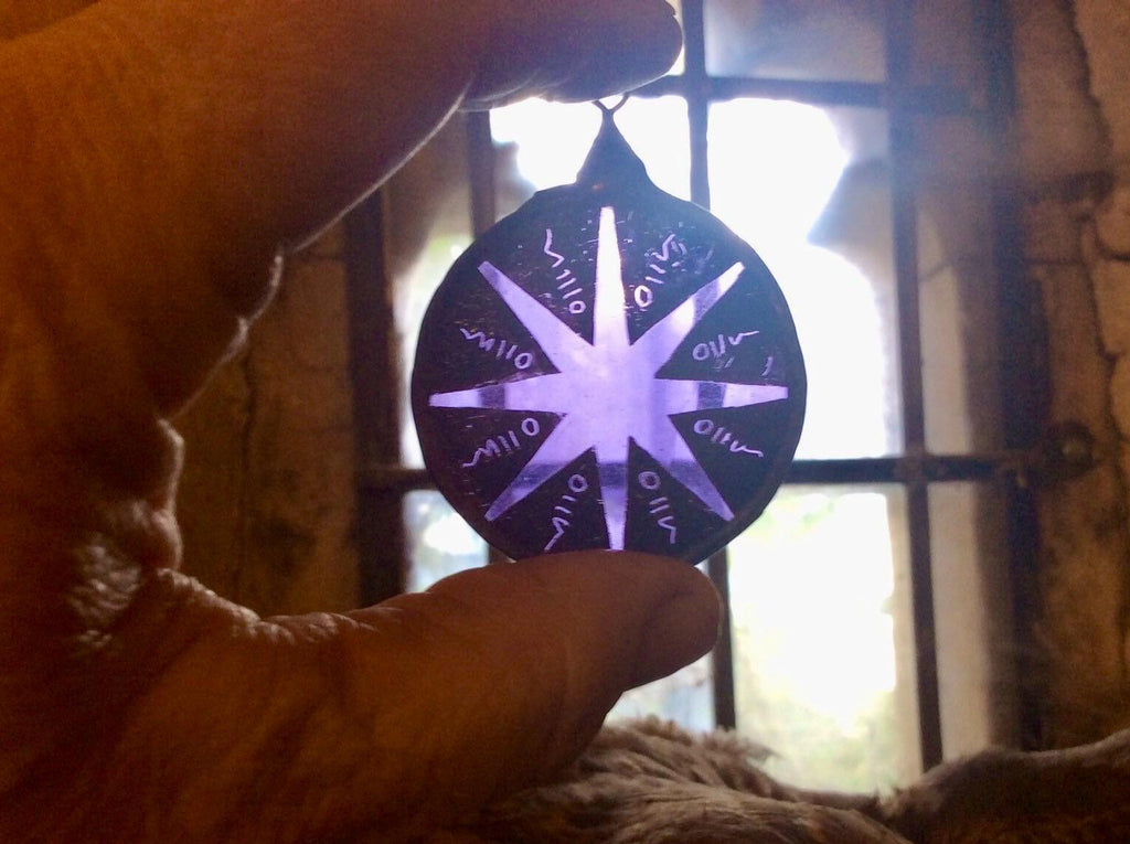 Hand holding a round purple stained glass star decor with against a blurred background of a vintage window