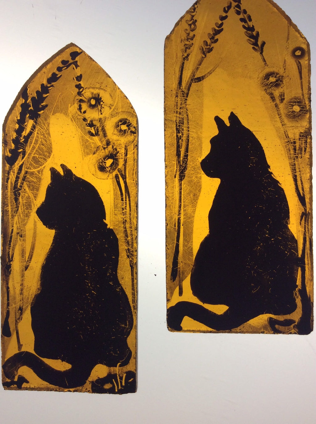 Two decorative arched stained glass  panels each with a black silhouette of a cat and dog on an amber background.  Shown on a light box