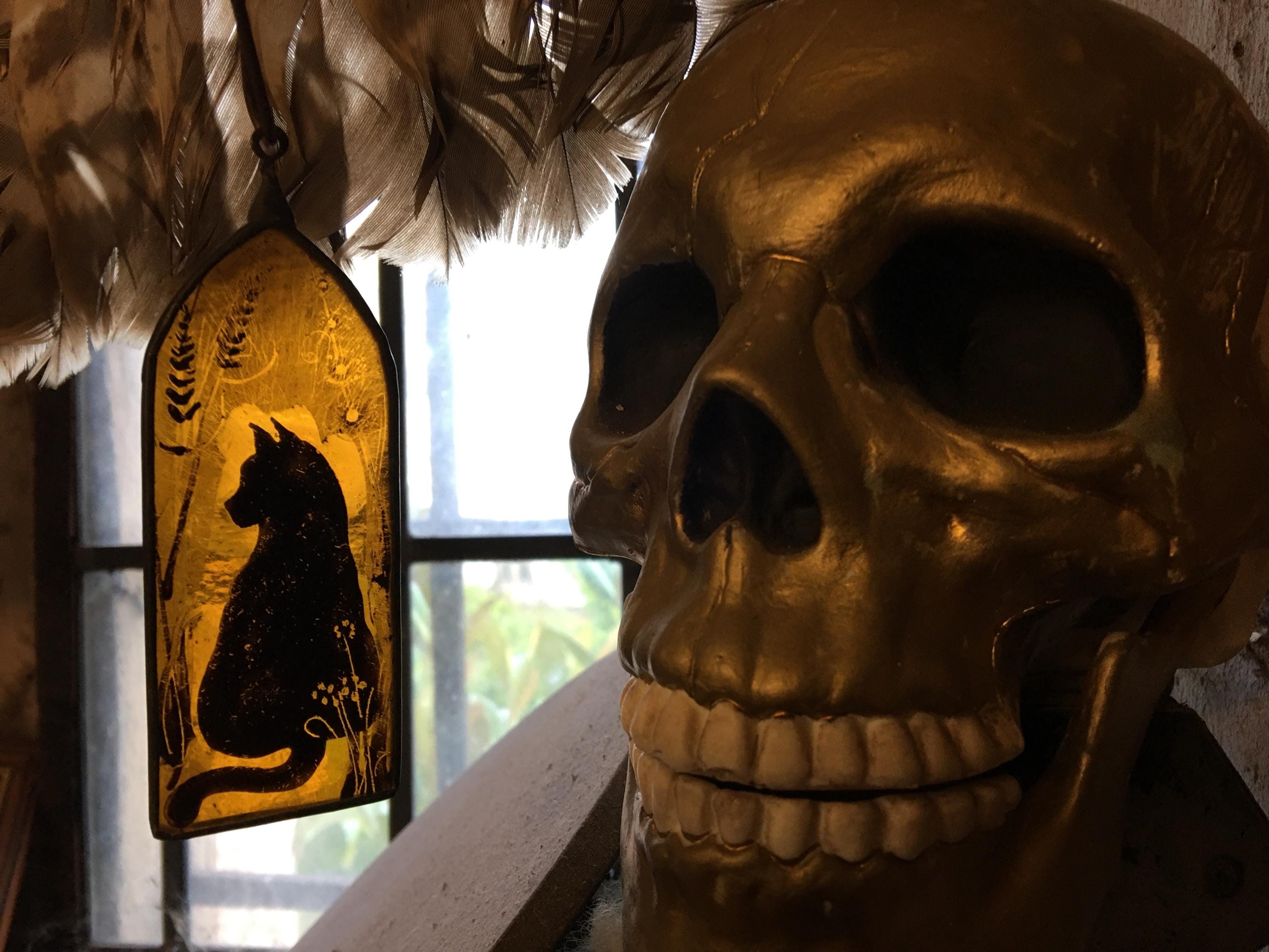 Gold skull decoration with a stained glass panel featuring a cat silhouette.