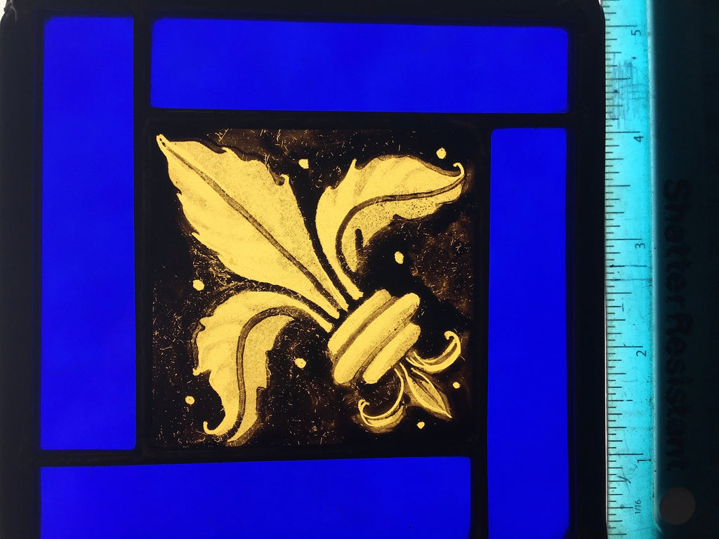 Decorative gold coloured glass with a hand painted design on a blue background with a ruler for scale.