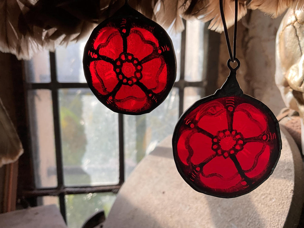 Two different red Tudor rose stained glass sun catchers hanging in a sunny window