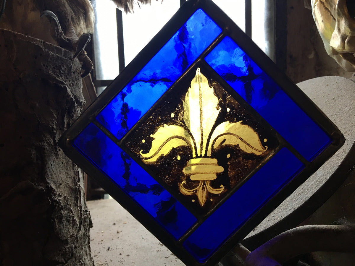 Stained glass panel with gold fleur-de-lis design on a blue background