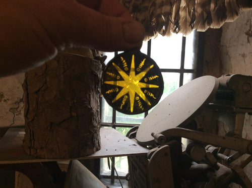 Close-up of a decorative stained glass star sun catcher with silver stained yellow centre and black border, held by a hand.