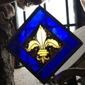 Stained glass panel with gold fleur-de-lis design on a blue background