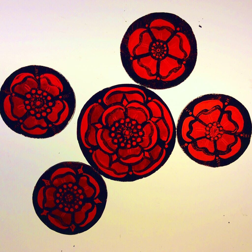 Five red Tudor rose designs on black circles against a white light box