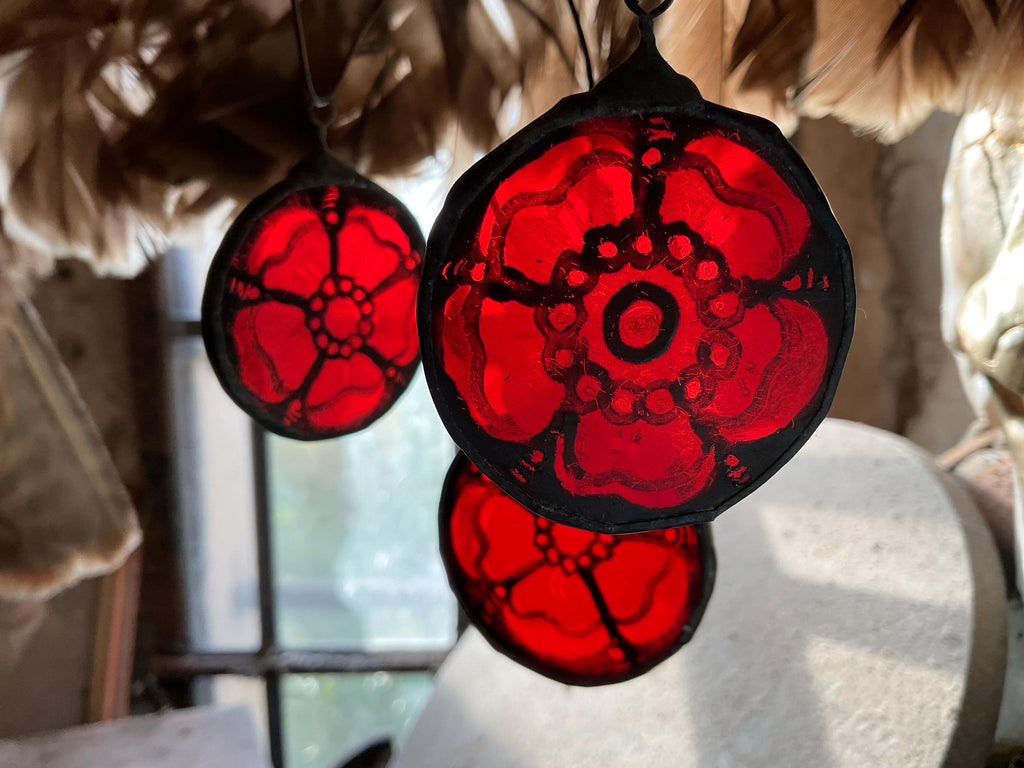Three stained glass red roses of Lancaster hanging in low light by a window with feathers