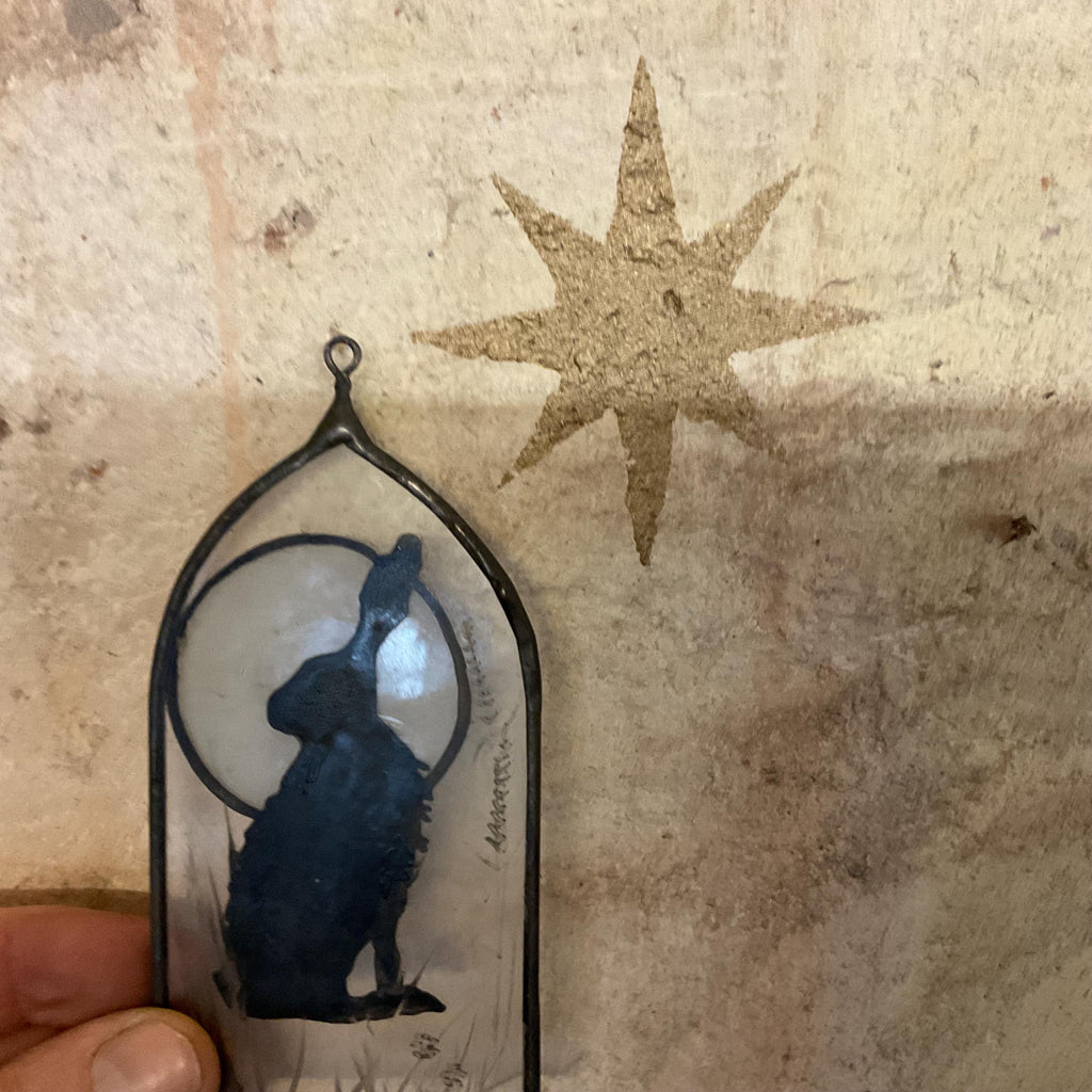 Decorative stained glass and enamel artwork with a silhouette of a rabbit and a star on a textured background