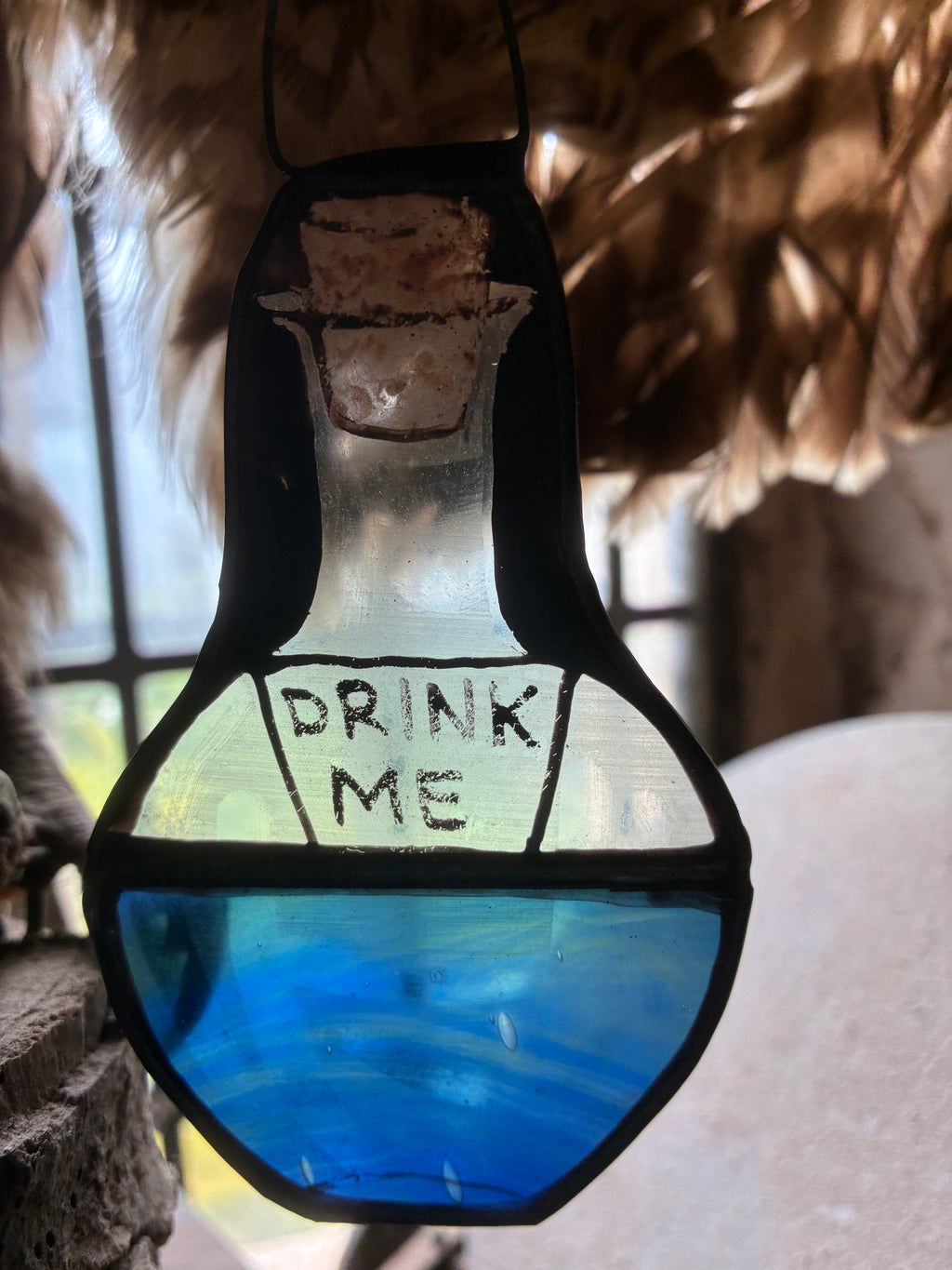 Sun Catcher of a bottle with 'Drink Me' text in a glass container, surrounded by natural elements.  Inspired by Alice in Wonderland