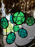 Green pentagram sun catchers hanging against a window with feathers.