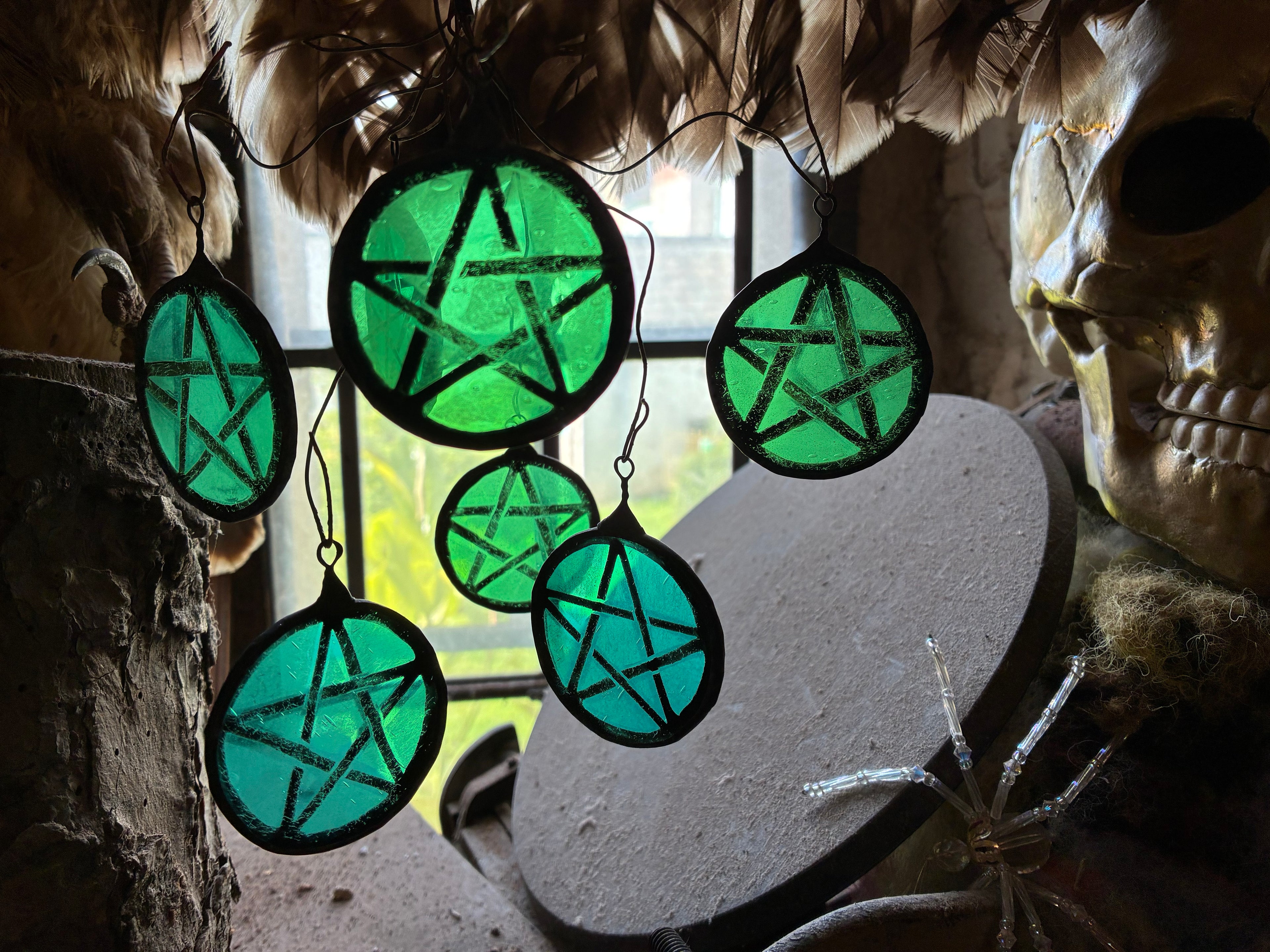Decorative green pentacle-shaped window hangings with a stone wall and skull in the background.