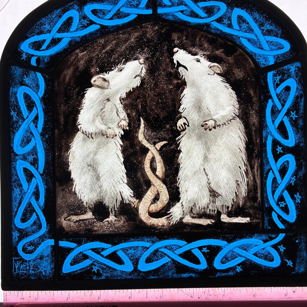 A square decorative stained glass artwork showing two white rats facing each other in a dark arched scene, framed by bright blue Celtic knot borders on a black background. A pink ruler is visible along the bottom edge for scale.