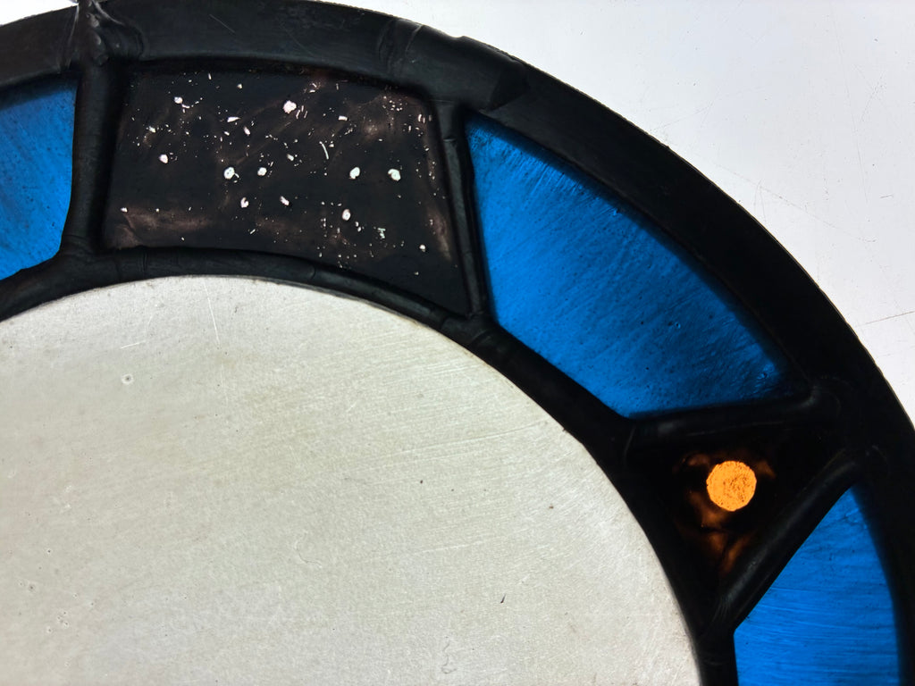 A close-up of a circular decorative moon with a large light gray centre, black segmented outer ring, bright blue panels, and a small amber/orange accent, depicting Mars photographed on a light box background.
