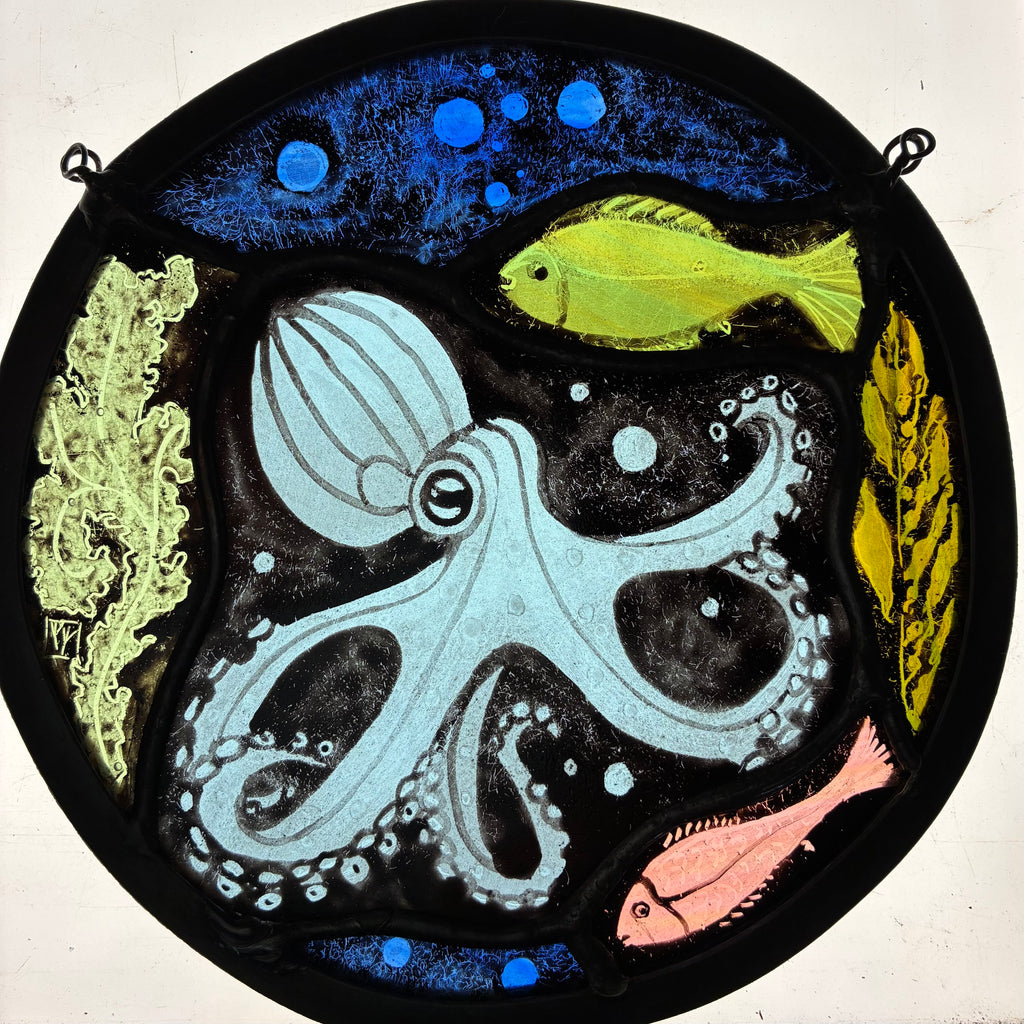 A circular stained glass window depicting an underwater scene with a light blue octopus, a green fish, a pink fish, and green coral against a dark background with blue bubbles.