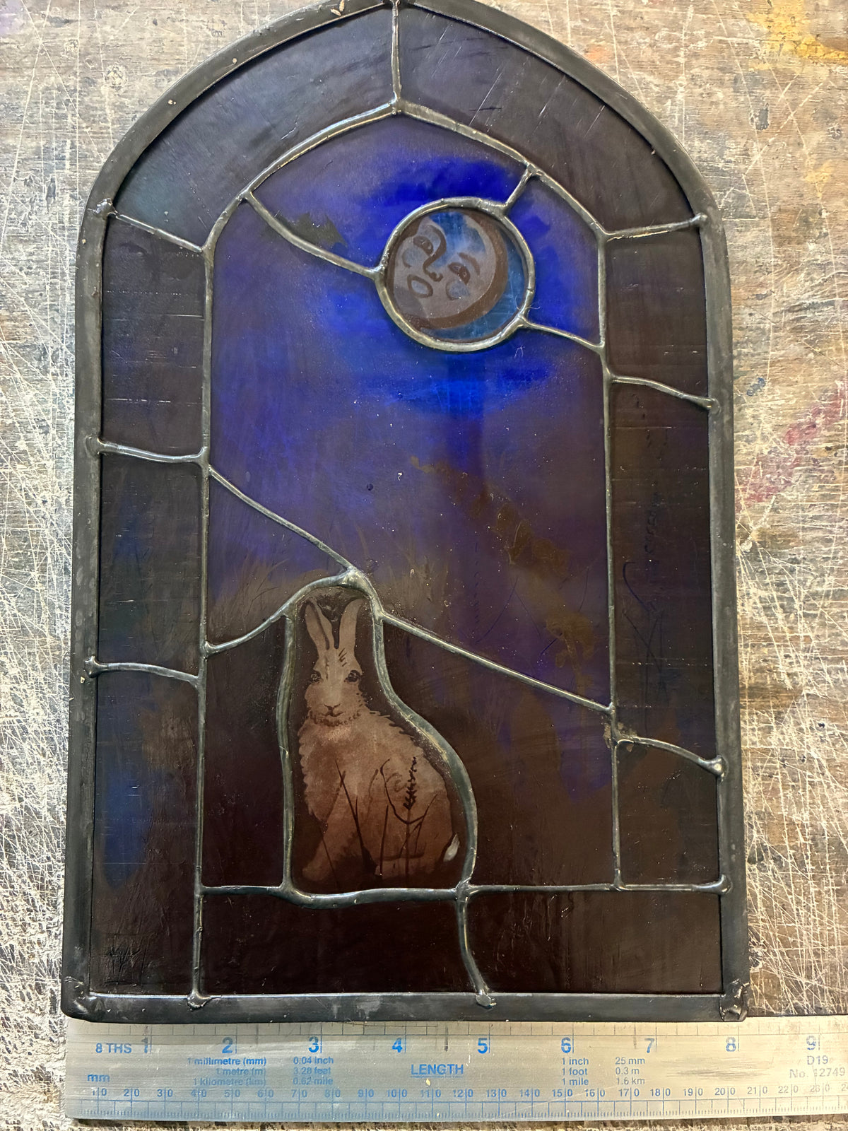 The arched stained glass piece showing the copperfoil construction and leaded border, with a ruler for scale 