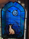 Hand-held stained glass window panel featuring a blue night sky with the new moon, a bat, a rabbit, and a foxglove silhouette, framed in dark metal.