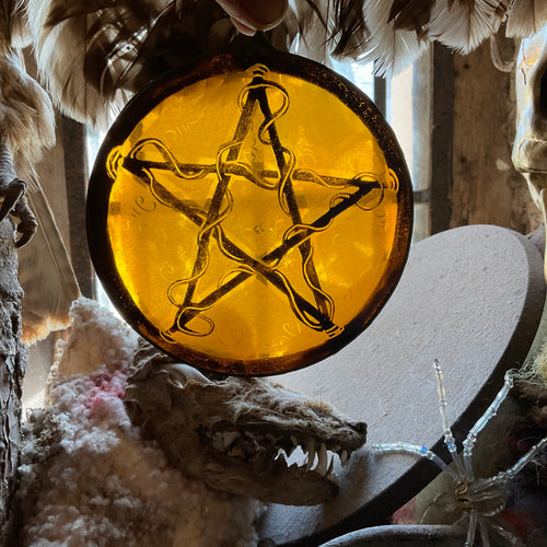 Amulet made from kiln fired painted stained glass with pentacle design on a warm yellow or amber  background, surrounded by mystical elements.