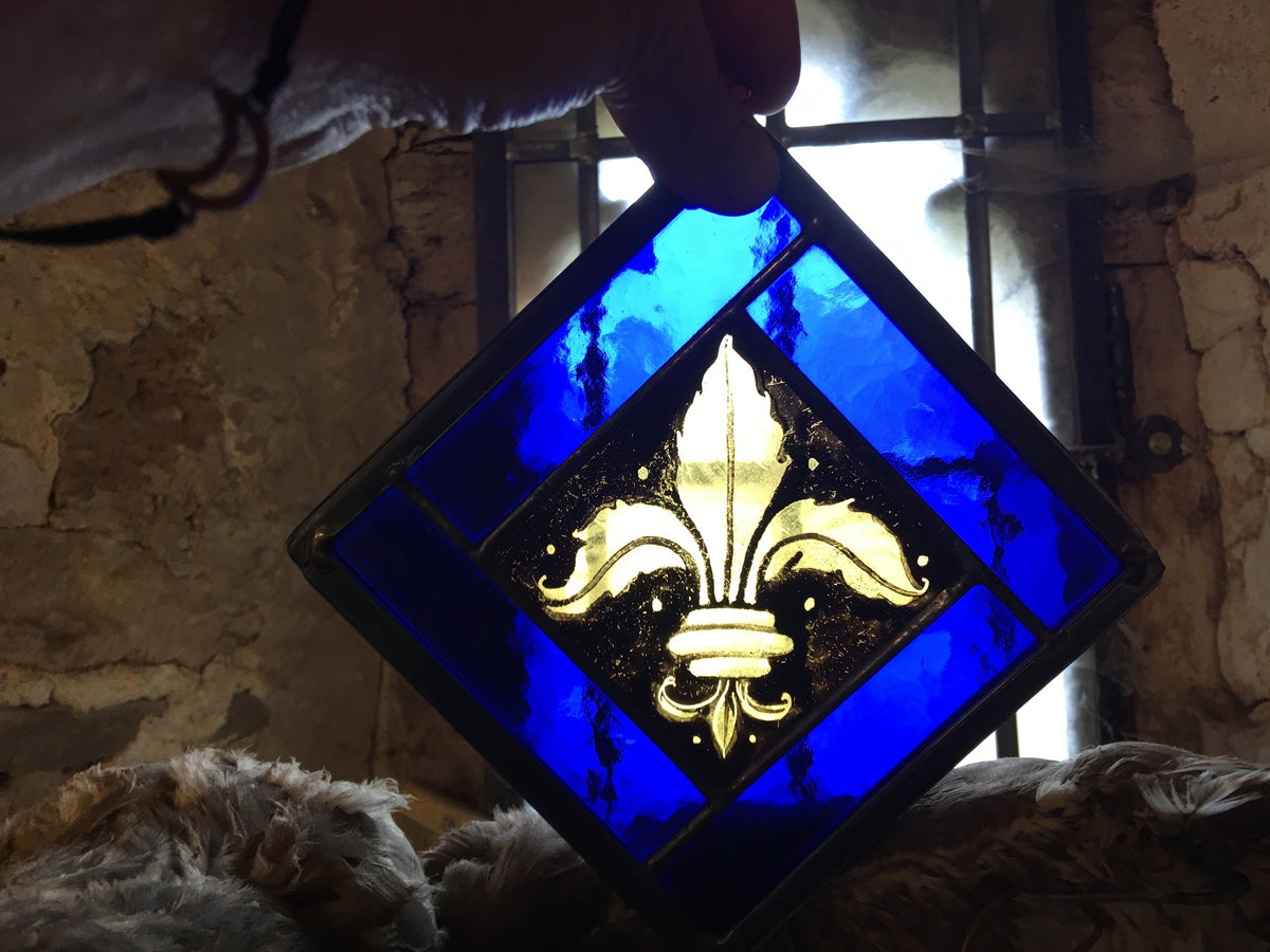 Hand holding a beautiful fleur de Lys motif on yellow glass with a simple blue border 