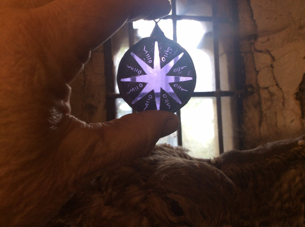 Close-up of a hand holding a glowing purple stained glass star decor in front of a window with stone walls.