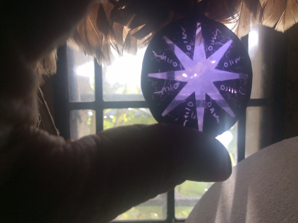 Held stained glass piece with star design and little details, shown against feathers and a vintage window in the background