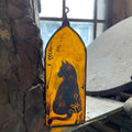 Decorative glass panel with a silhouette of a cat on a yellow background, leaning against a stone wall.
