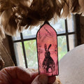 Decorative pink pendant with a rabbit design held by a hand, with feathers and a blurred background.