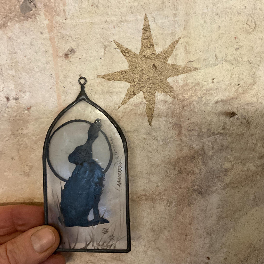 Up cycled glass arch with hare and moon enamelled, held by the hand which made it in front of an old wall with a gold star