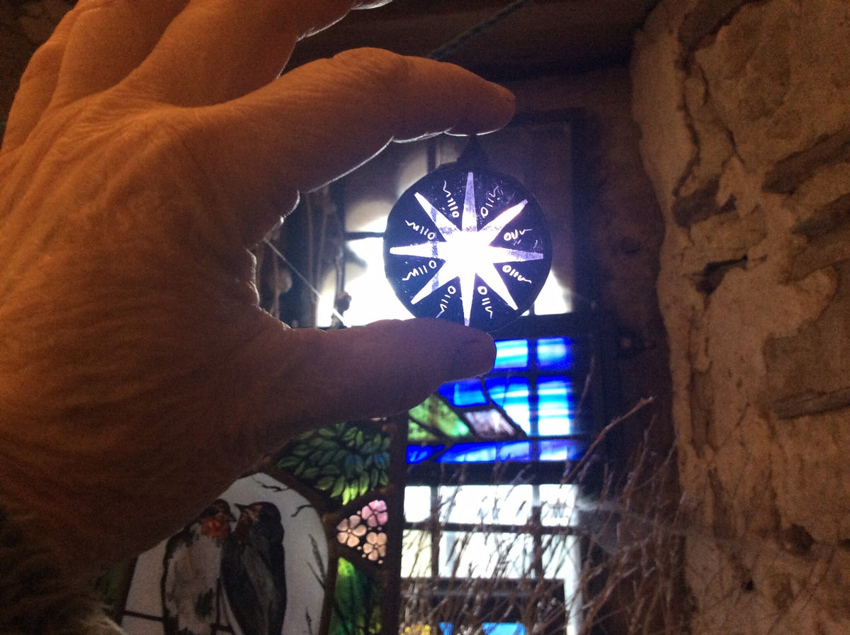 Hand holding a stained glass star sun catcher in front of a bright sunny window to show scale