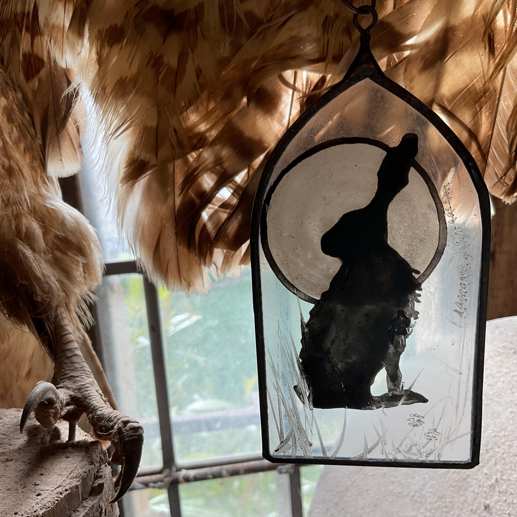Decorative glass panel with a silhouette of a hare and moon and feathers in the background