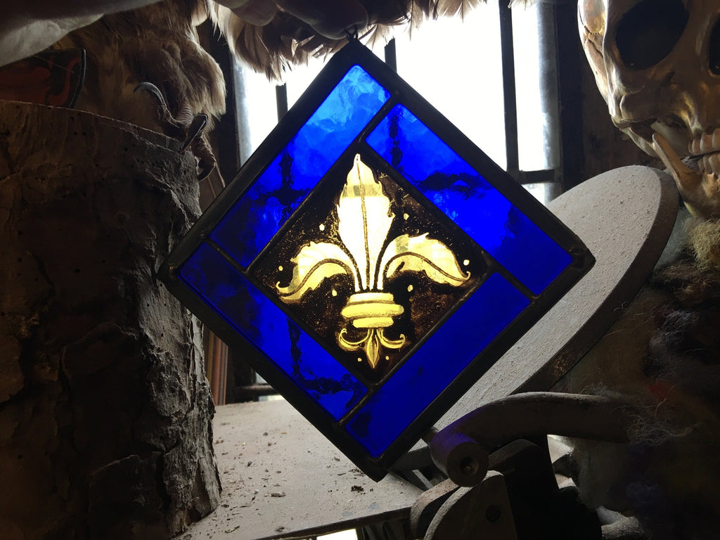 Stained glass panel with a gold fleur-de-lis design on a blue background, held by a person.