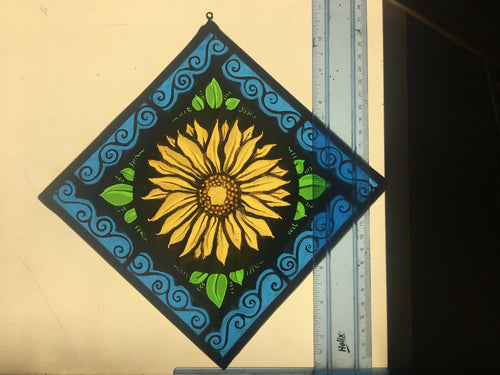 Decorative stained glass panel with a sunflower design on a light box with a ruler for scale