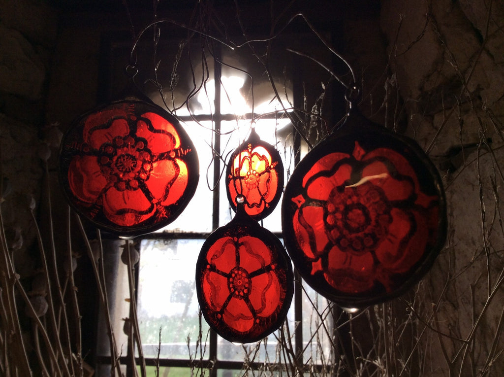 Decorative red Lancastrian rose stained glass hangings against a dark background with a window.