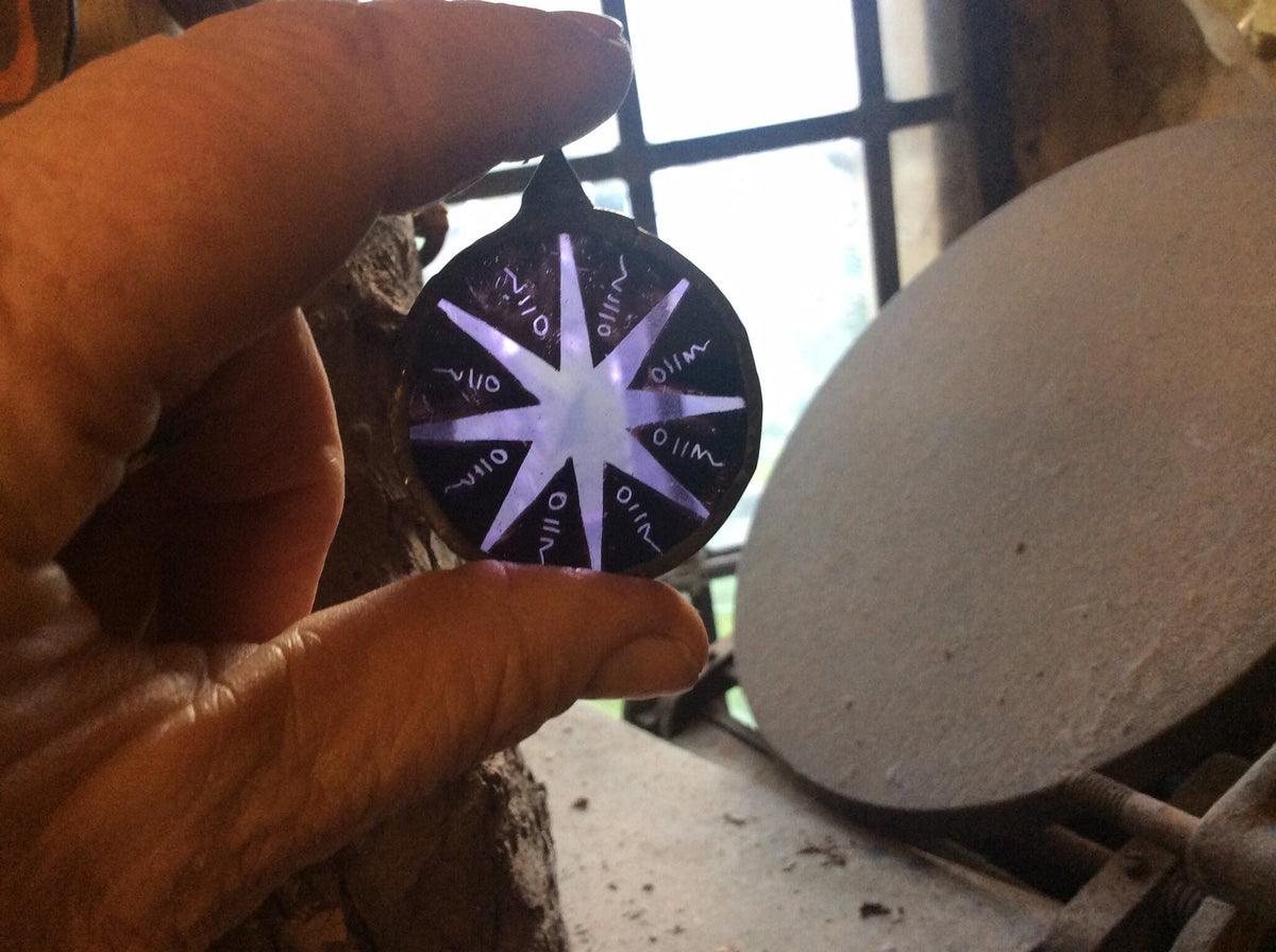 Hand holding a round, painted and kiln fired stained glass star with a purple light pattern against a studio background