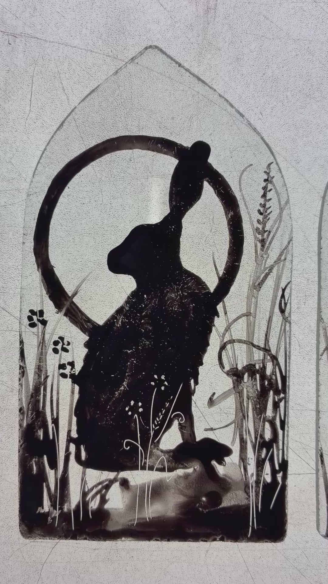 Six pieces of glass on a light box painted with the hare and the hollow of the moon before the first kiln firing, and the tools used for painting and sgraffito.